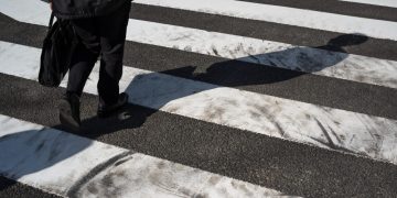 Uma senhora com um vaso atravessa a rua