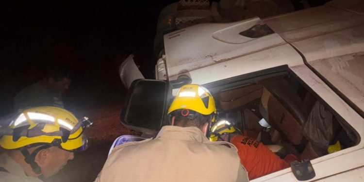 Carreta com soja tomba e motorista fica presa às ferragens